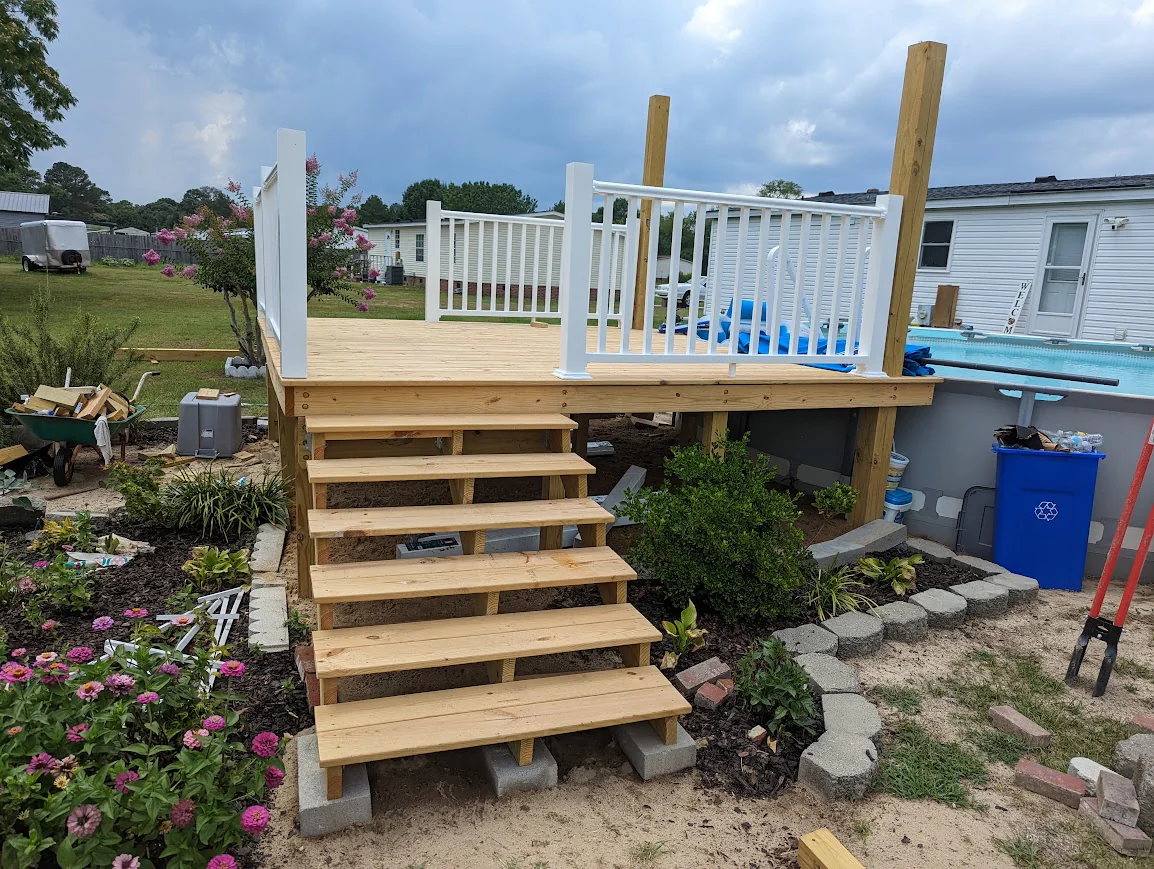 New wooden deck with white railings and stairs beside an above-ground pool